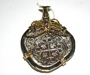 A close-up of an Atocha Shipwreck Necklace Pendant with a 14K gold lobster clasp. The pendant features a round silver centerpiece with intricate patterns and a small gold piece at the top, symbolizing the treasure that was salvaged from the famous shipwreck. The pendant is suspended from a delicate silver chain and would make a unique and meaningful addition to any jewelry collection